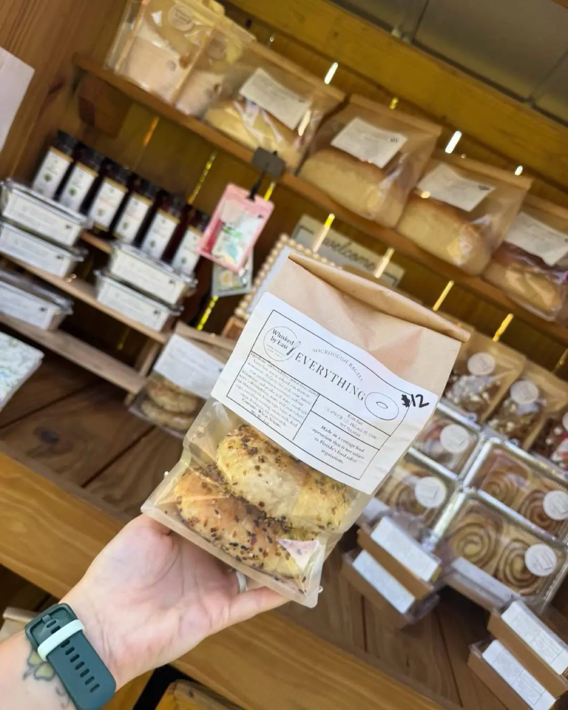 A kraft bag of Everything sourdough bagels held up in front of the stand shelves