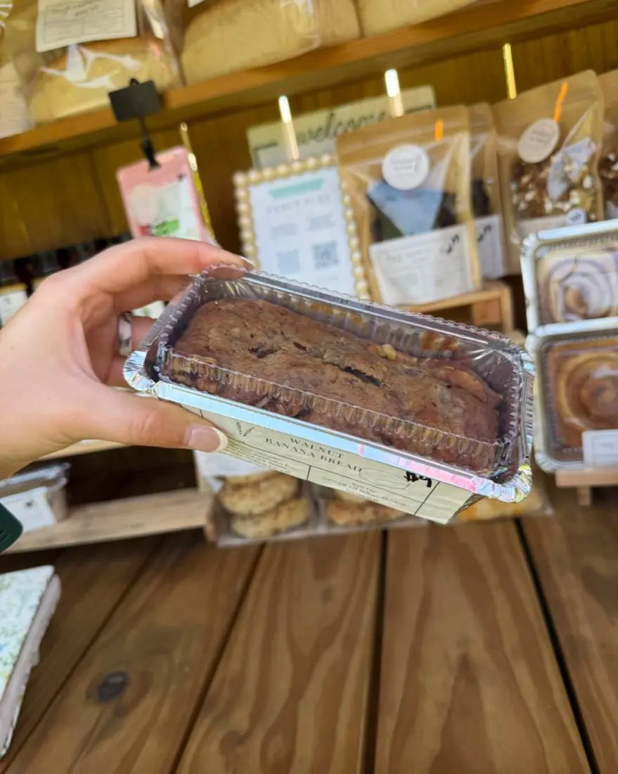A walnut banana bread in a foil loaf pan, held up in front of the stand shelves