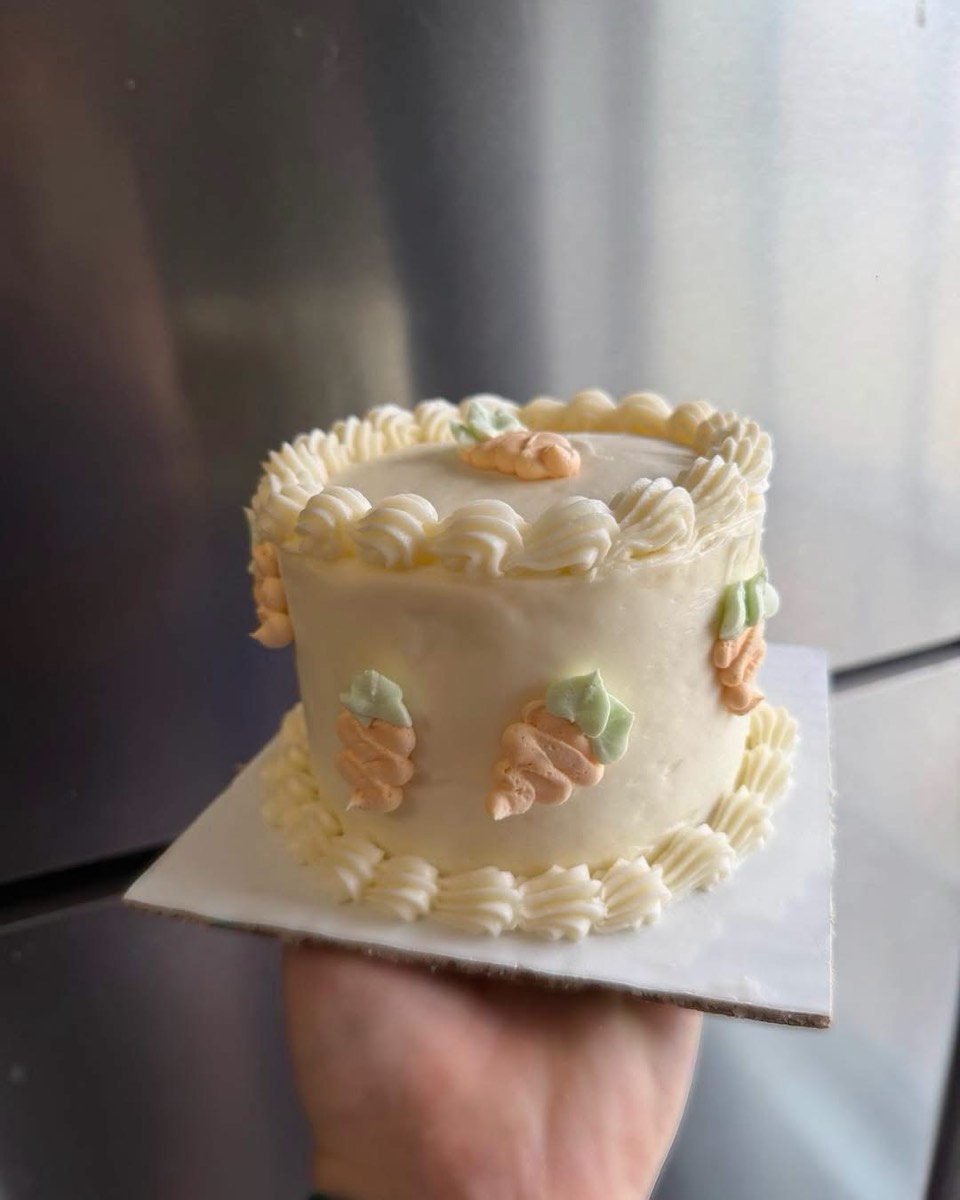 A small carrot cake with shell piping and piped carrots, held on a board