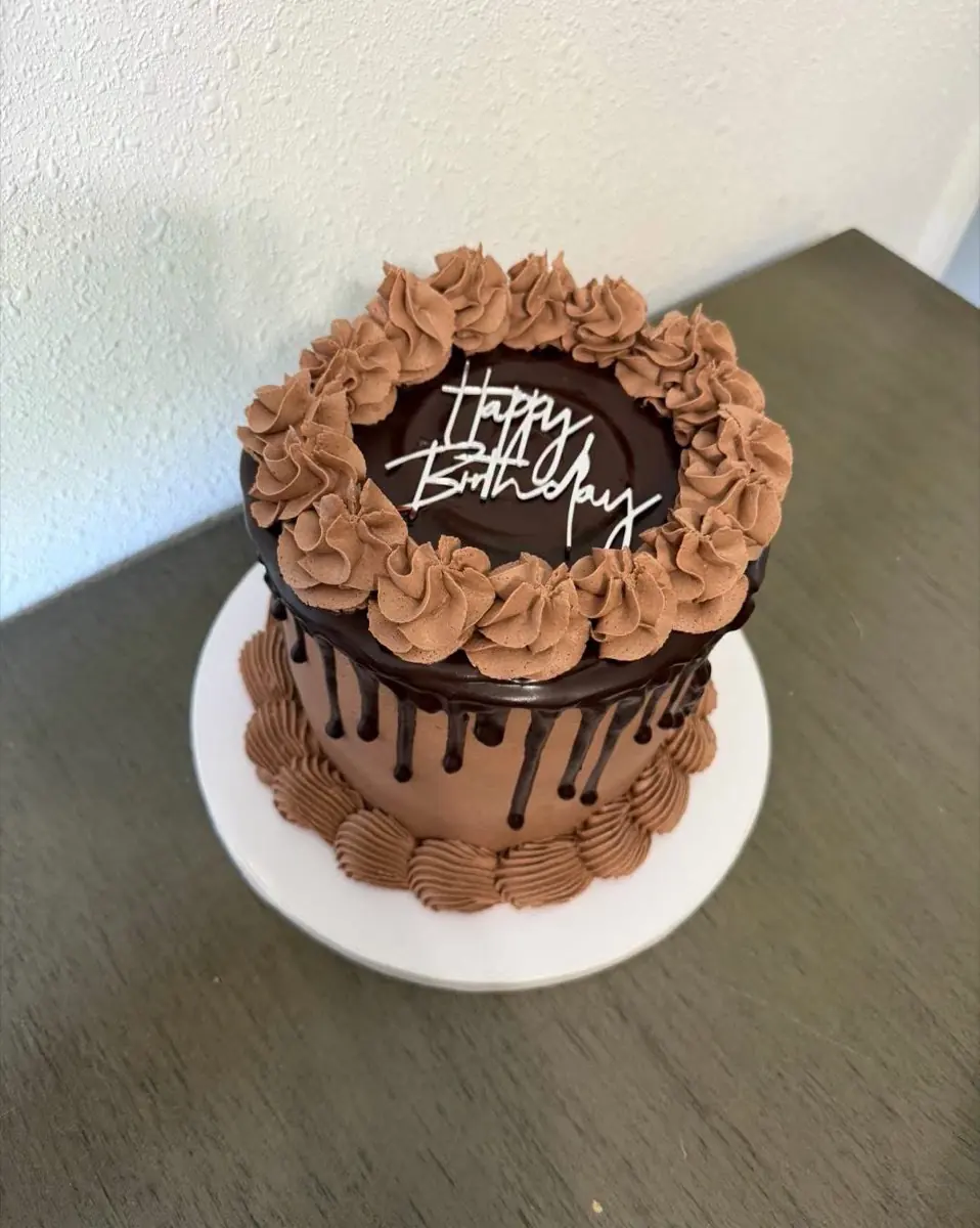 A chocolate buttercream cake with a ganache drip, piped rosettes and a Happy Birthday topper