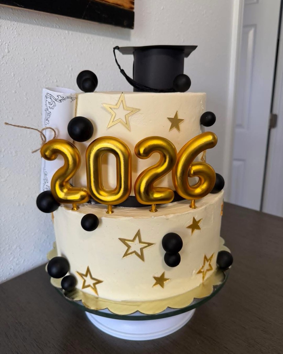 A two-tier ivory buttercream graduation cake with gold 2026 numerals, gold stars and black spheres