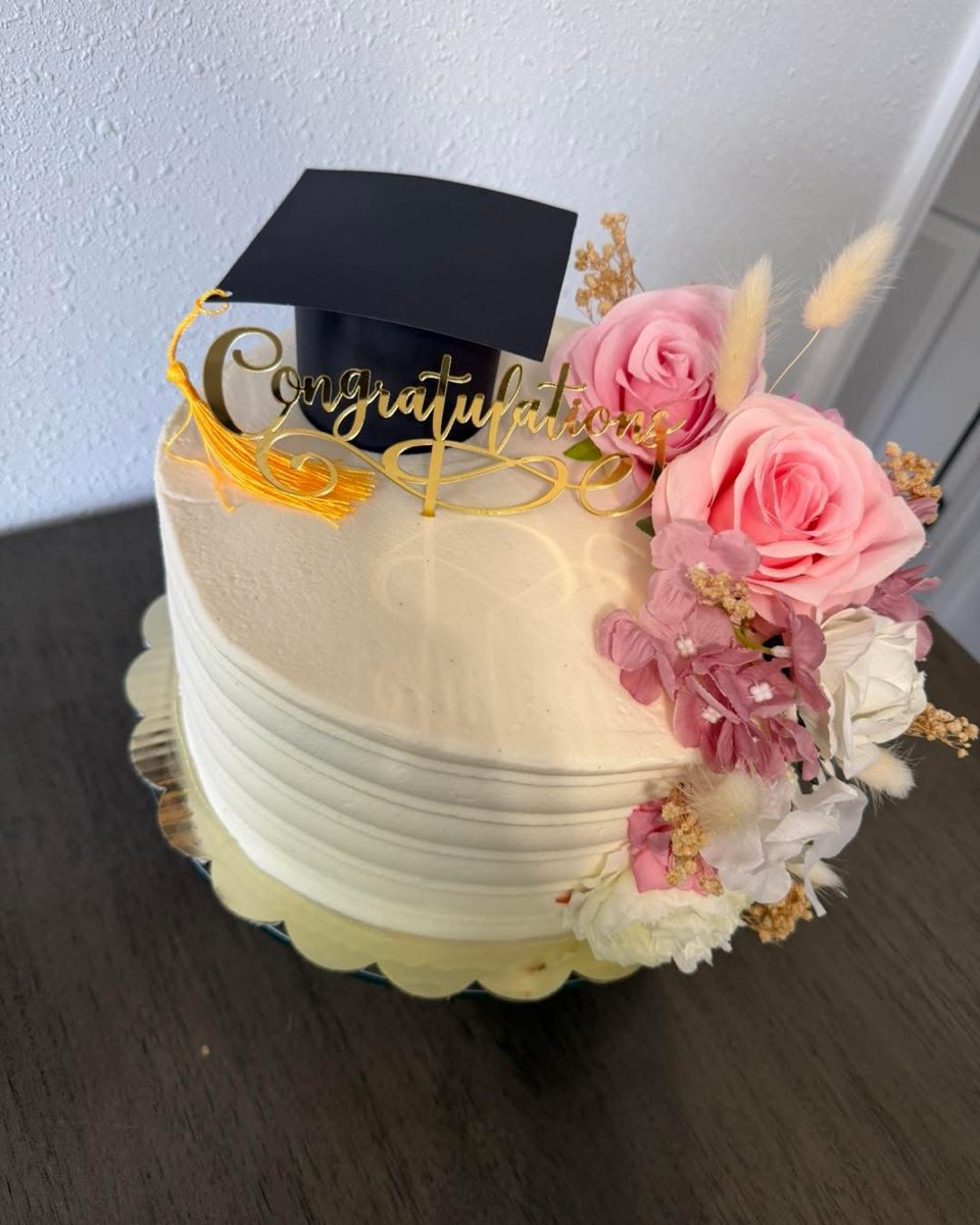 A white buttercream graduation cake with a mortarboard topper and pink roses