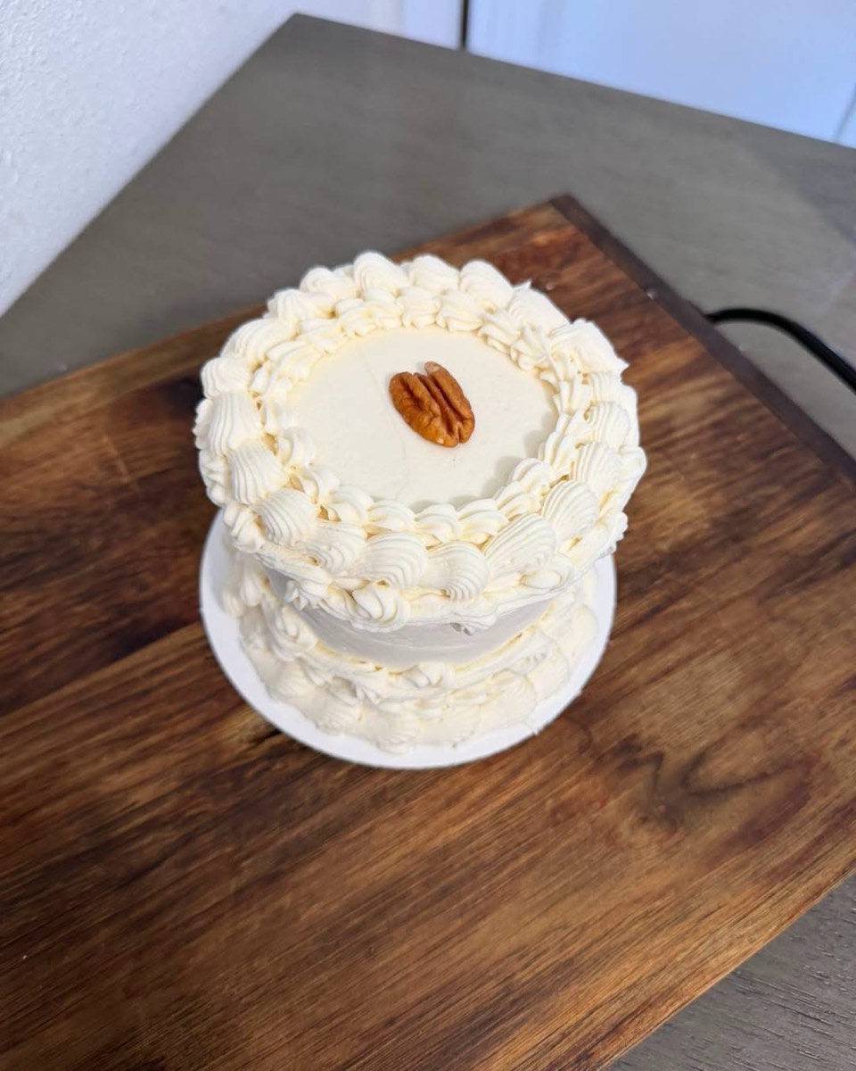 A pale buttercream cake with shell piping and a single pecan on top