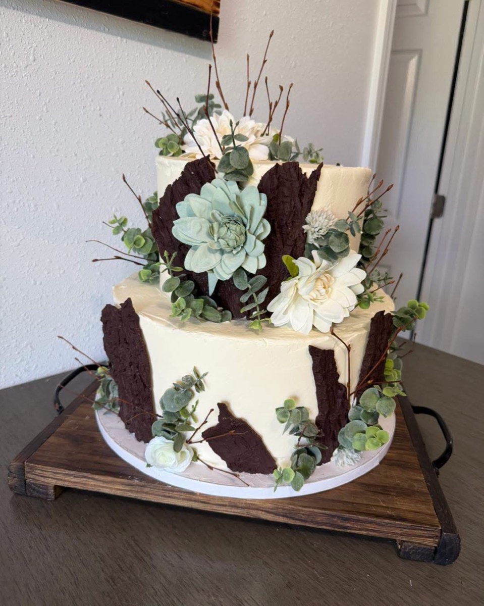 A two-tier buttercream cake with chocolate bark panels, succulents, eucalyptus and white blooms
