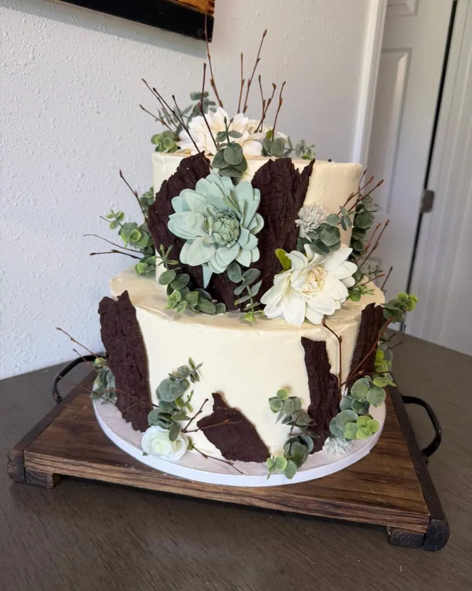 A two-tier buttercream cake with chocolate bark panels, succulents, eucalyptus and white blooms