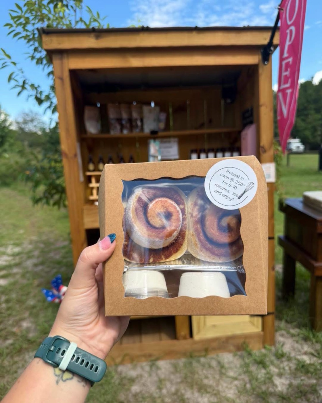 A boxed pair of cinnamon rolls with icing cups, held in front of the farm stand