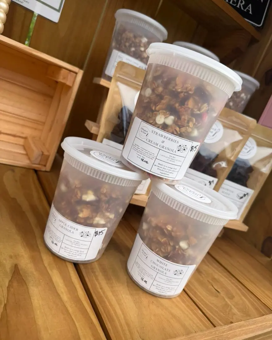 Stacked 12 oz tubs of granola labelled Strawberries & Cream, Apple Cider and White Chocolate