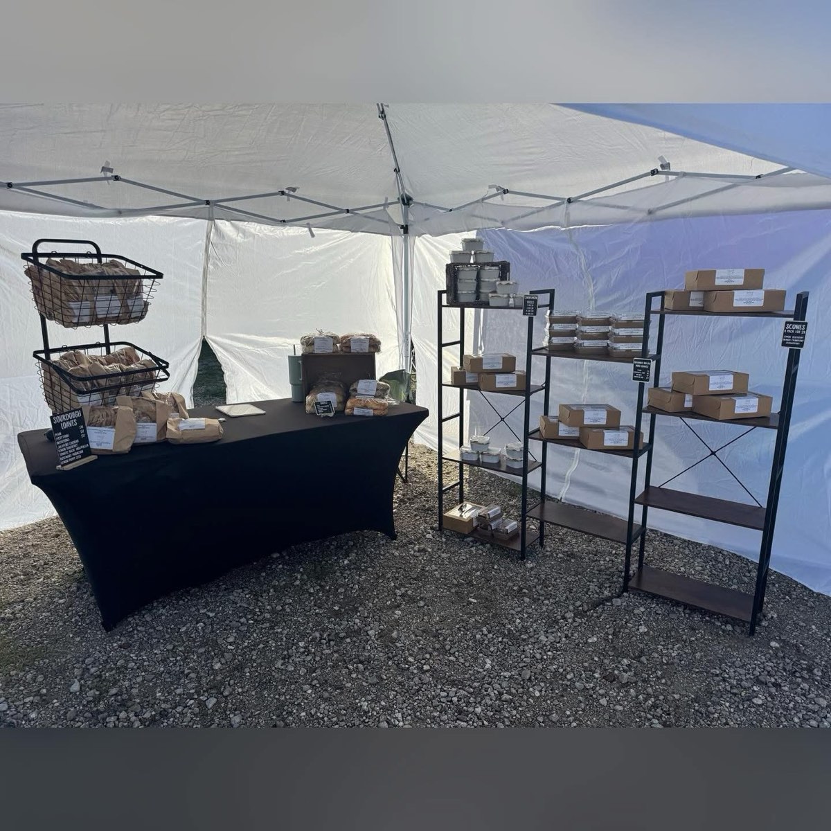 The Whisked by East market booth under a white tent, with baskets of bagged sourdough and a price board