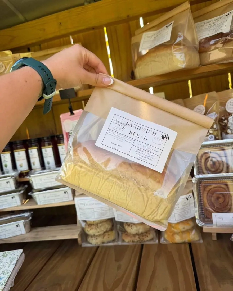 A bagged loaf of sandwich bread held up in front of the stand shelves