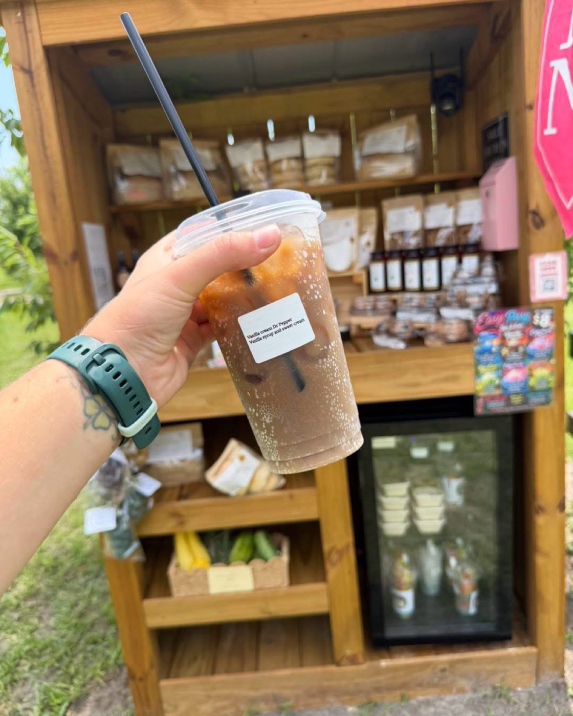 A vanilla cream Dr Pepper held up in front of the farm stand