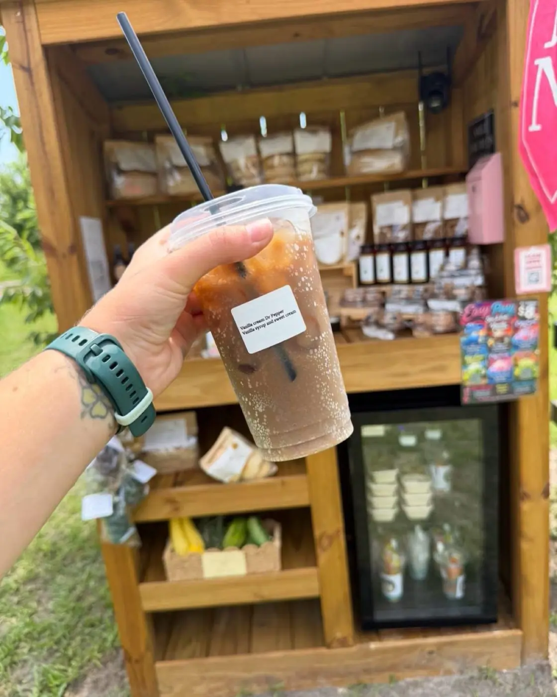 A vanilla cream Dr Pepper held up in front of the farm stand